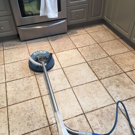 A blue floor-cleaning machine on a tiled kitchen floor with cabinets and a dishwasher nearby