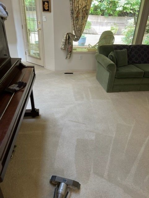 Living room with beige carpet being cleaned by a carpet cleaner near a green sofa and piano.