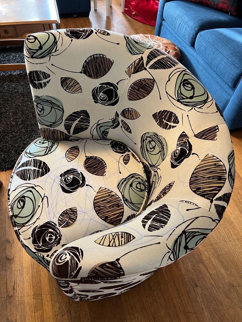 Patterned beige armchair with black leaf designs, sitting on a wooden floor beside a blue sofa.