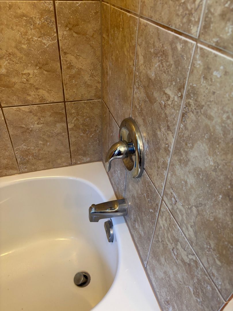 Bathtub corner with chrome faucet and tiled shower wall, white tub basin below.