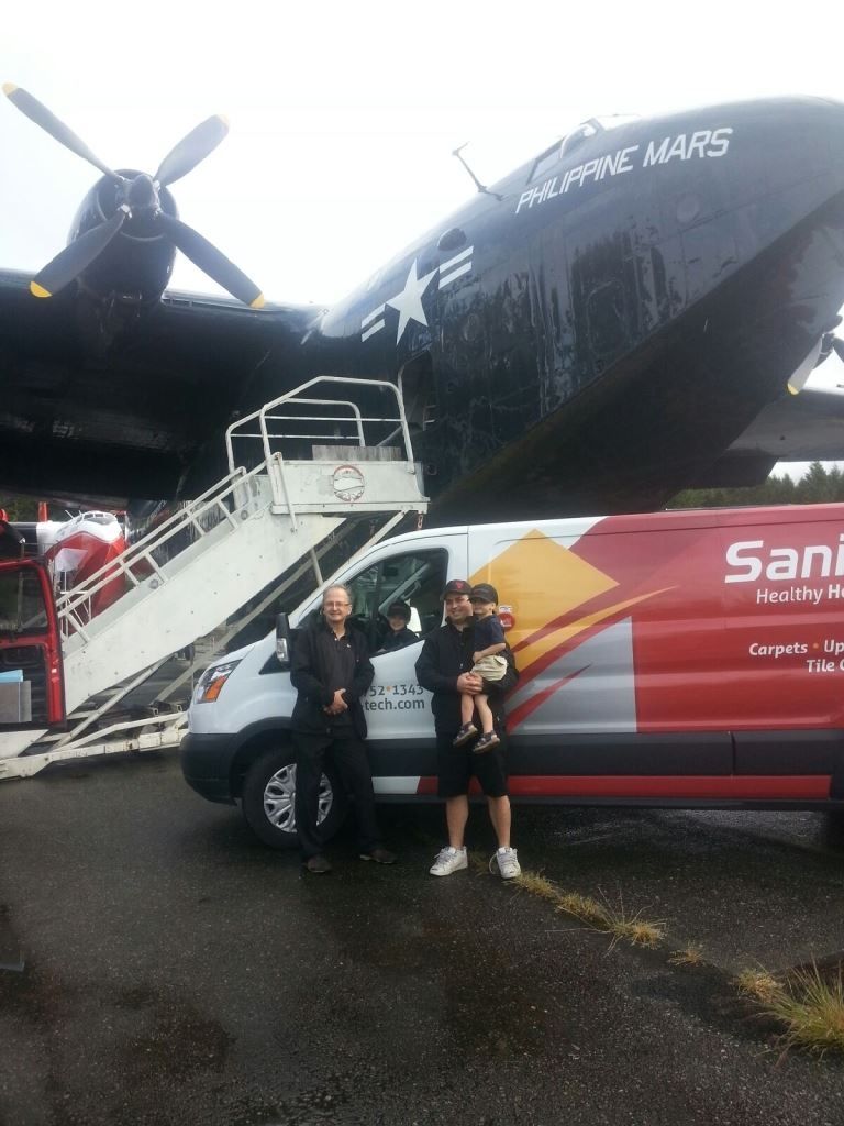 Two people standing beside a red San disk truck in front of a large black airplane on a wet tarmac