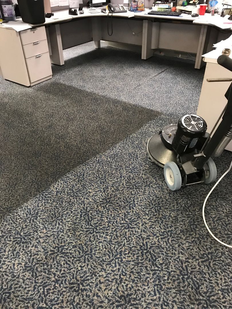Office carpet being cleaned with a floor buffer near desks and cabinets