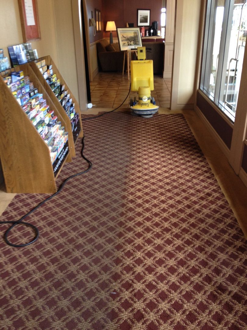 Empty hotel hallway with patterned carpet, brochure rack on the left, and a yellow floor-cleaning machine ahead