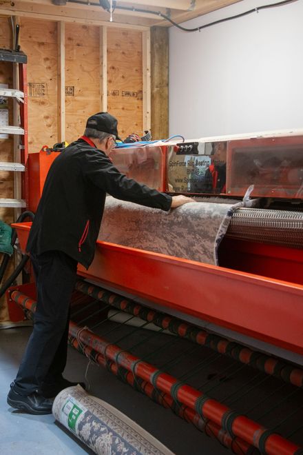 Worker operating a red industrial machine in a workshop, with rolls of material nearby.