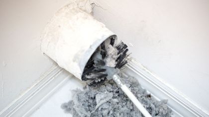 Dustpan holding spilled gray debris in a corner beside a white wall and baseboard.