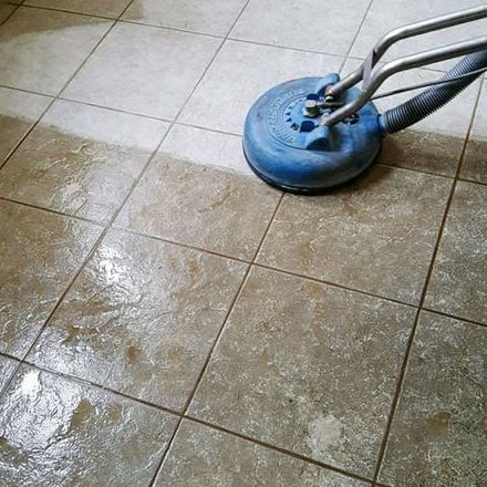 Blue floor-cleaning machine scrubbing a tiled floor, leaving a wet, cleaned area behind