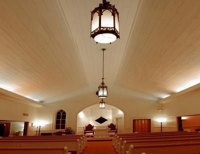 Empty church sanctuary with wooden pews, arched ceiling, and hanging lanterns