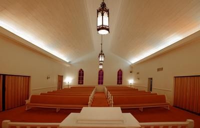 Empty church sanctuary with wooden pews, central aisle, and hanging lanterns under a vaulted ceiling