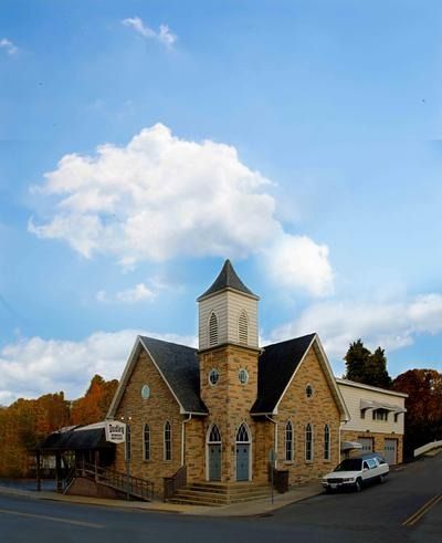 Stone church with a central tower on a street corner under a blue sky with clouds