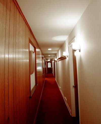 Narrow red-carpeted hallway with wood-paneled walls and wall lights, stretching into the distance