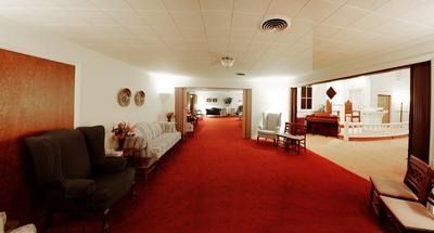 Long red-carpeted hallway with chairs, tables, and a lounge area in a bright interior.