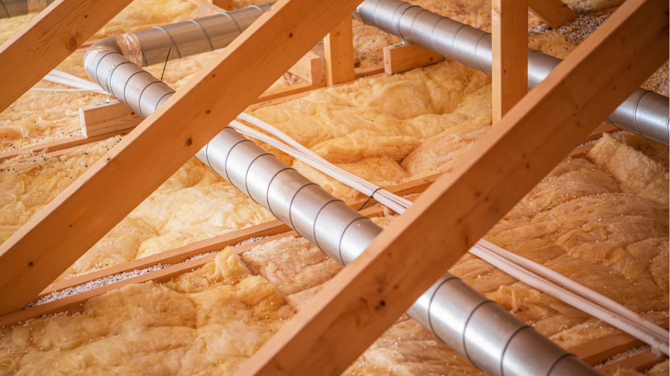Attic with wooden beams, insulation, and silver ductwork.