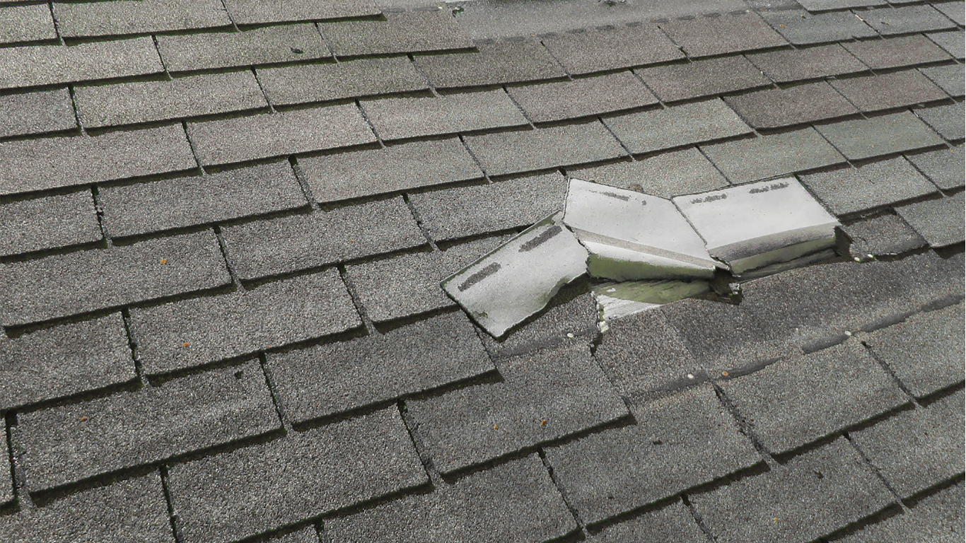 Damaged asphalt shingle roof. White flashing is torn and exposed.