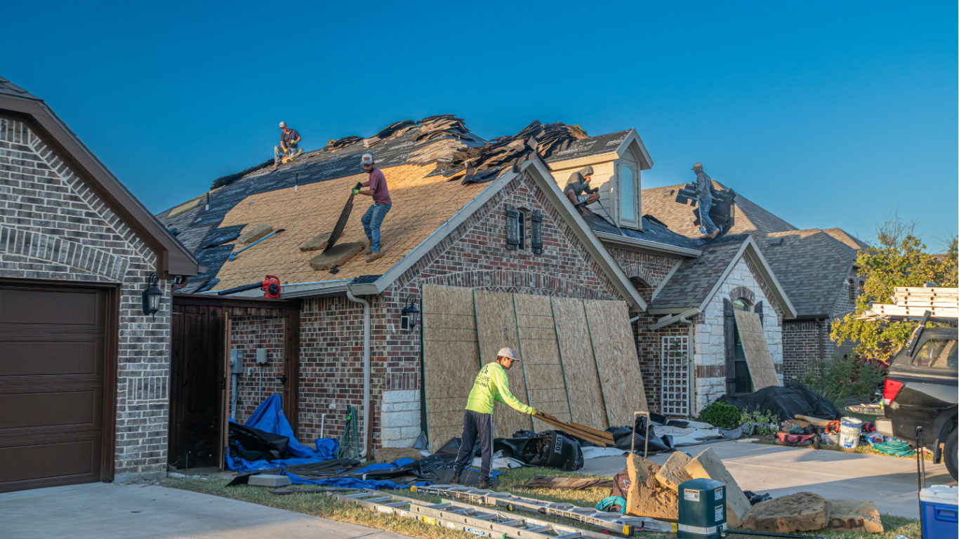 Roofers working on a residential roof, removing old shingles and preparing for new ones.