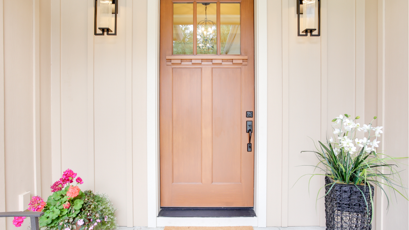 Wooden front door with sidelights, two wall sconces, and flower pots.