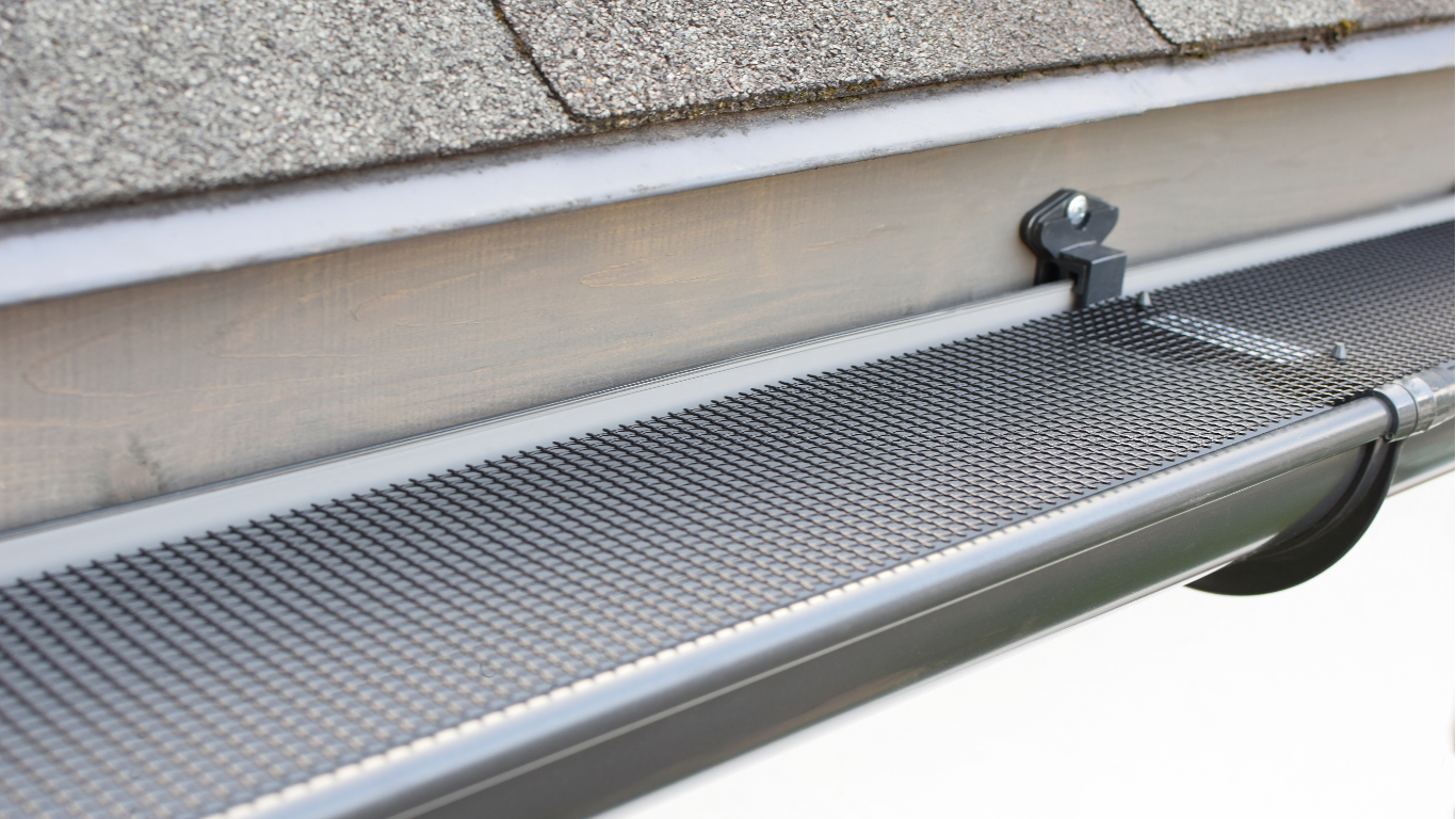 Gutter with black mesh guard, attached to a roof with shingles.