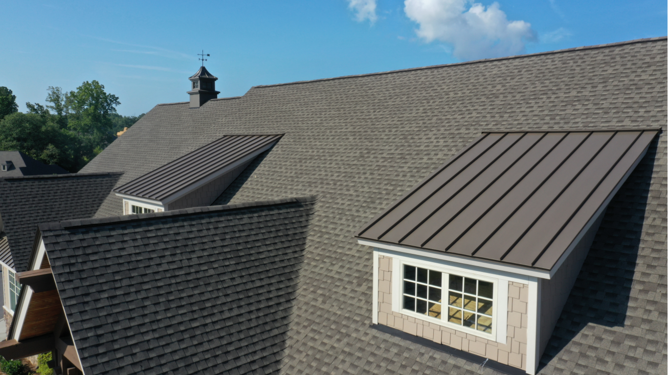Brown shingled roof with a dormer featuring a brown metal roof and white framed windows.