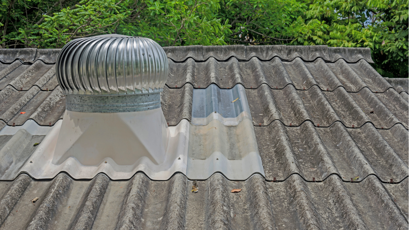 Roof with a silver rotary vent. Gray tile roofing, green trees in background.