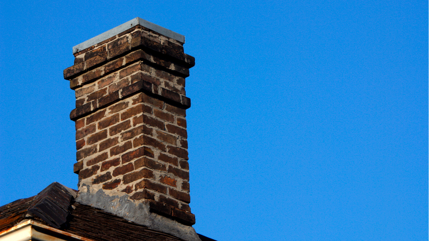 Brick chimney on a rooftop against a clear blue sky.