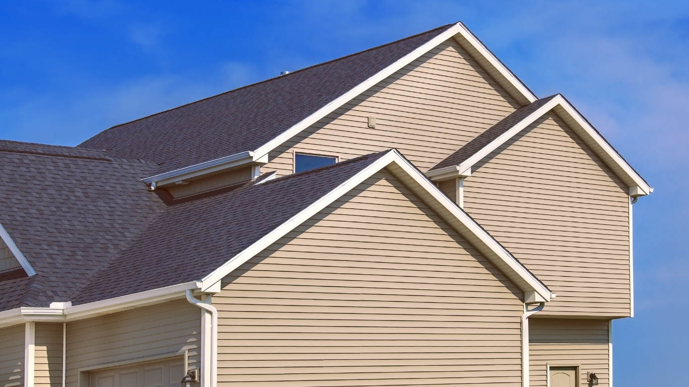House exterior with dark roof and beige siding against a blue sky.
