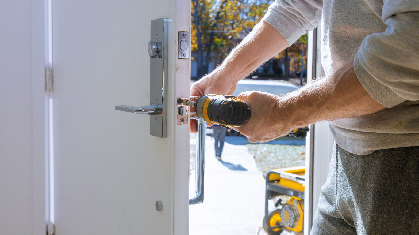 Person using a power drill to install a door handle on a white door.