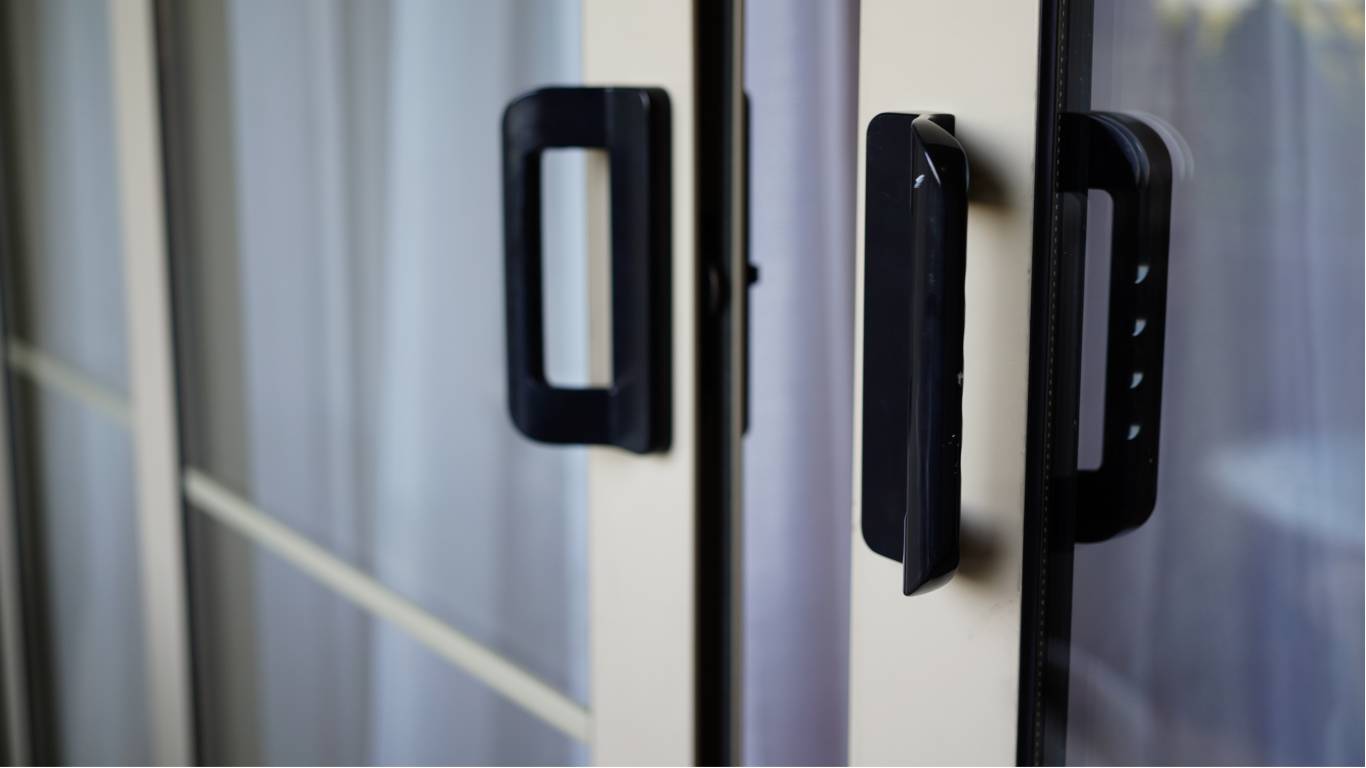 Black handles on a white double door, with a blurred background of a curtain.