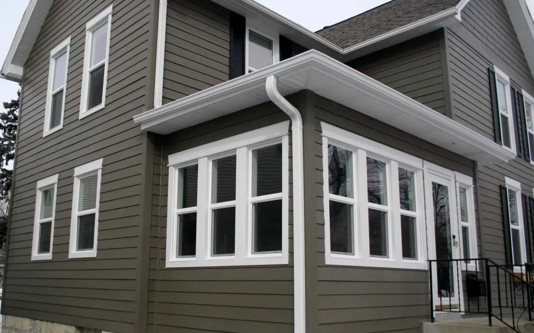 Two-story house with green siding, white trim, and a sunroom with large windows.