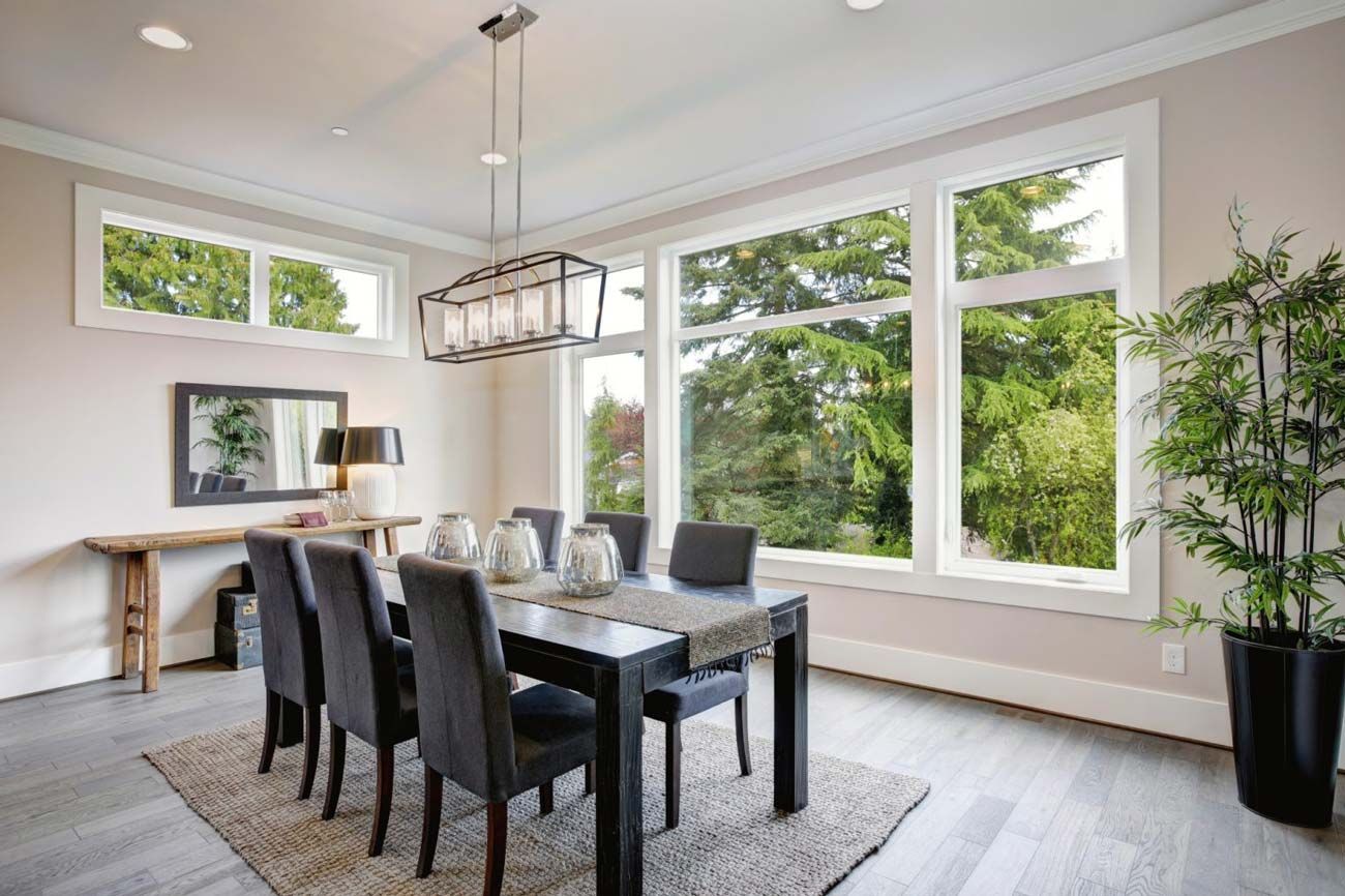 Dining room with a table, chairs, large windows, and a plant.