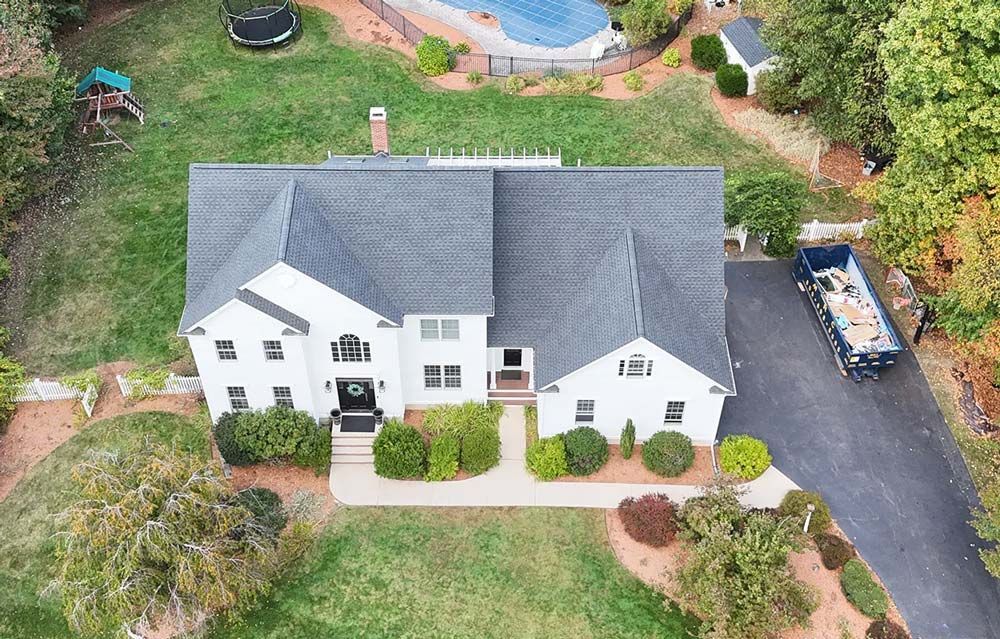 Aerial view of a white two-story house with a dark gray roof, driveway, and pool.