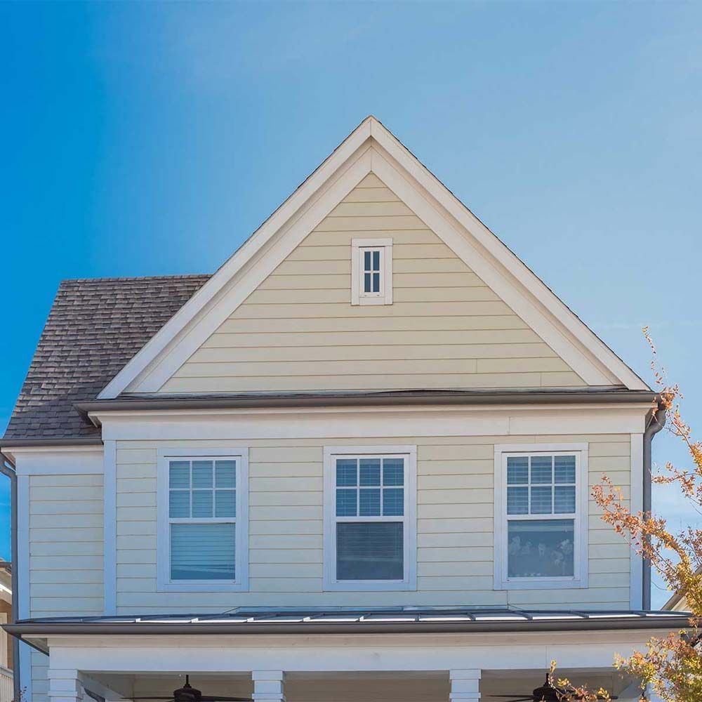 Two-story house with light yellow siding, white trim, and a gray roof against a clear blue sky.