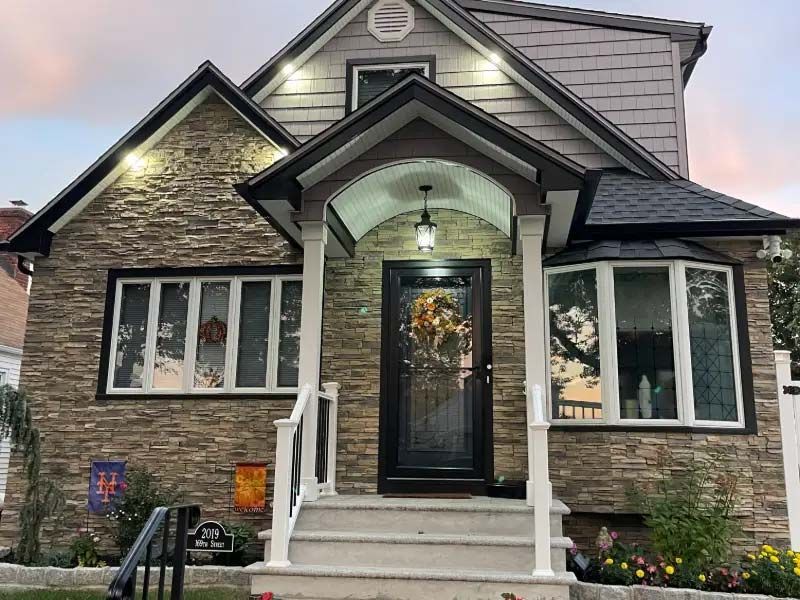 Stone-faced house with porch and black door, under a dusk sky.