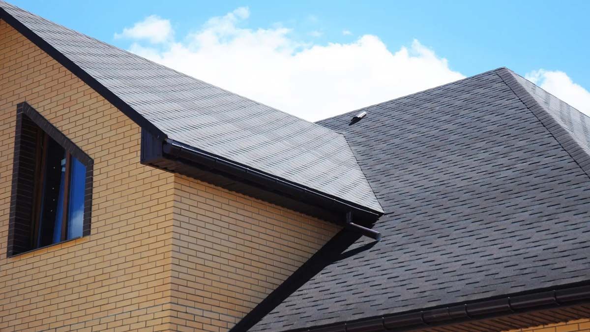 Brick house with a dark gray shingled roof, brown trim, and a blue sky.
