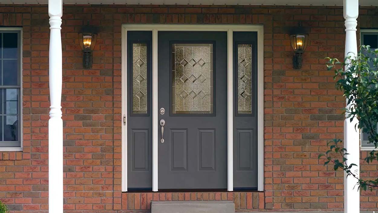 Gray front door with sidelights, set in brick. Two porch lights flank the door.