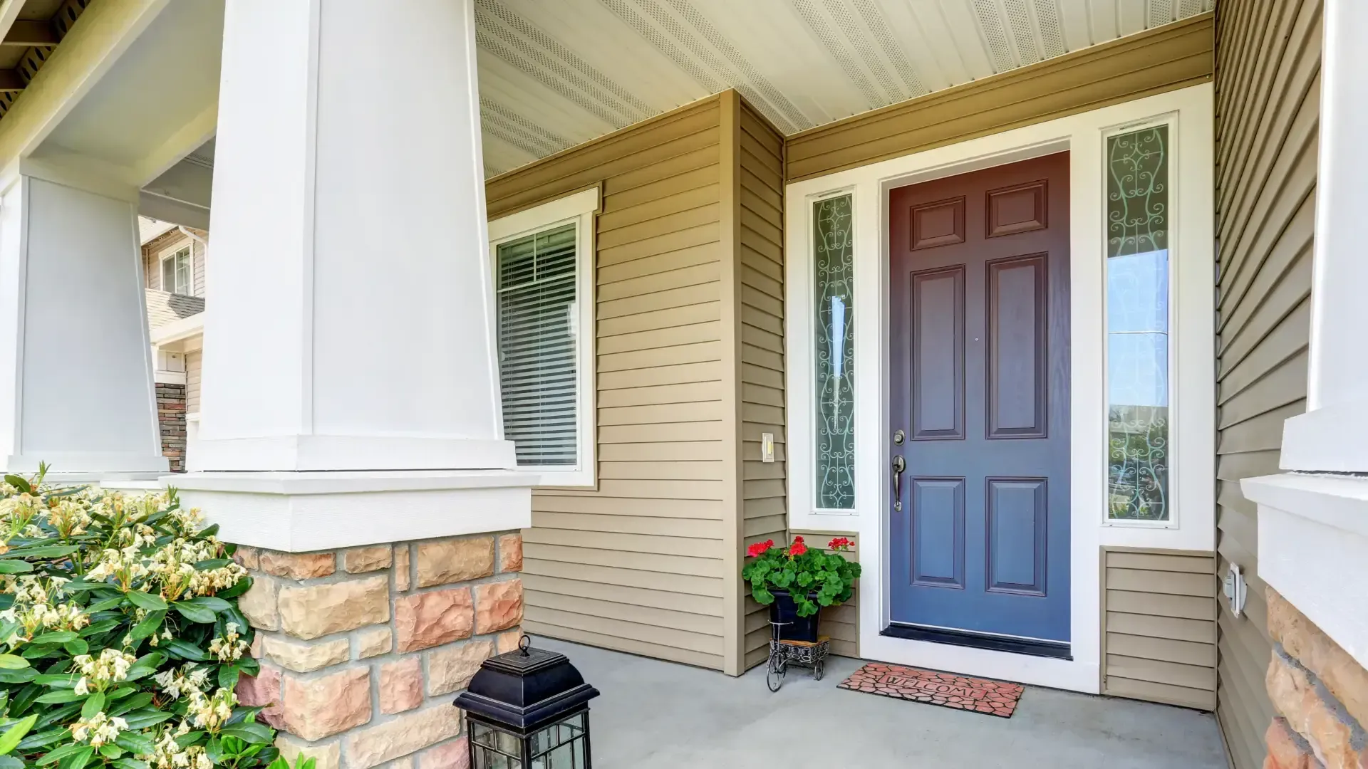 Blue front door with sidelights under a porch with white columns and tan siding.