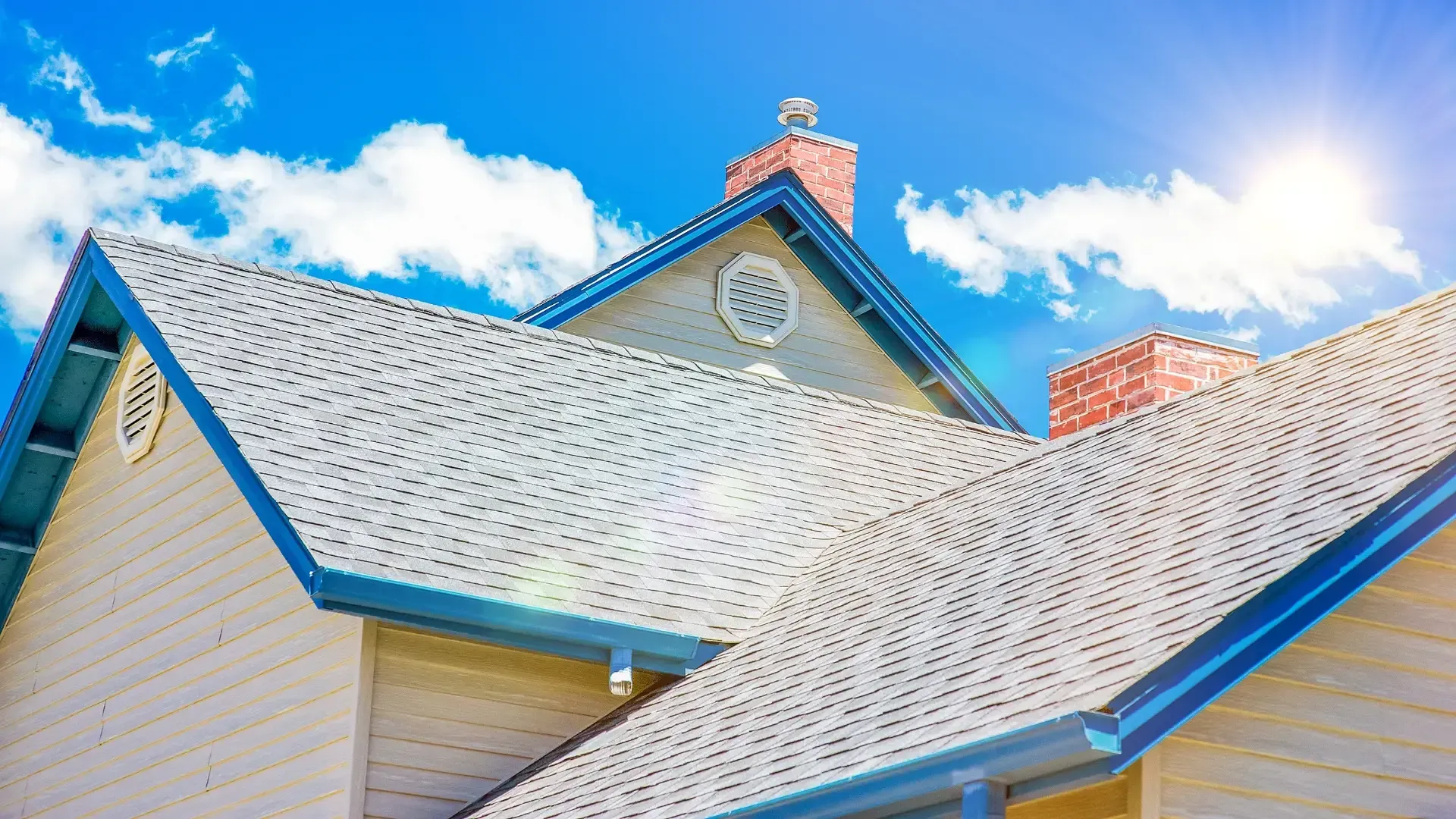 House with white roof, blue trim, and brick chimney against a bright blue sky with clouds.