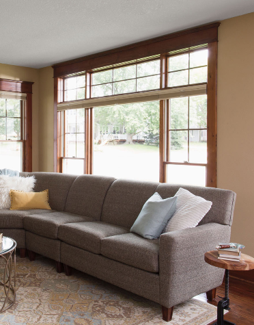 Brown sectional sofa in living room with large windows, brown trim, beige walls, and light rug.