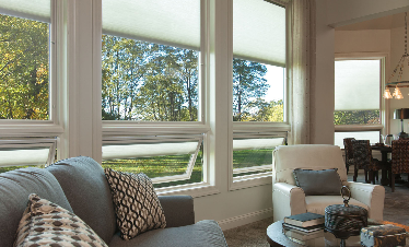 Living room with large windows, sheer shades, gray couch, white armchair, and outdoor view.