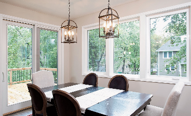 Dining room with dark table, six chairs, two pendant lights, and large windows overlooking a deck and trees.