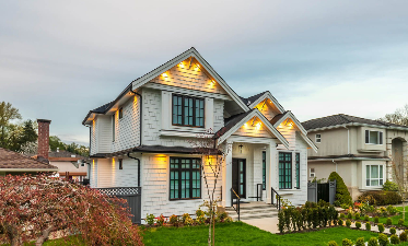 White two-story house with black trim, illuminated, set against a cloudy sky.