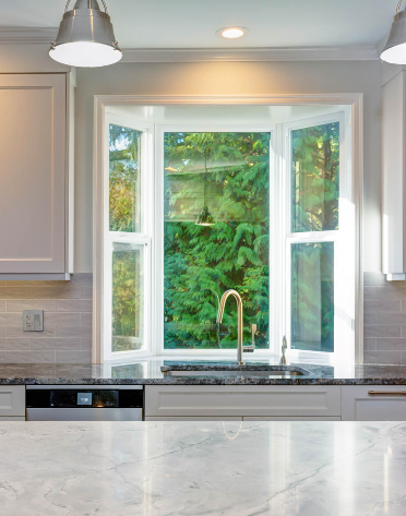 Kitchen with a bay window overlooking lush green trees, above a sink with a chrome faucet.