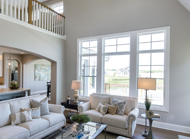 A bright, modern living room featuring cream sofas, a glass coffee table, and large windows looking onto a sunny yard.