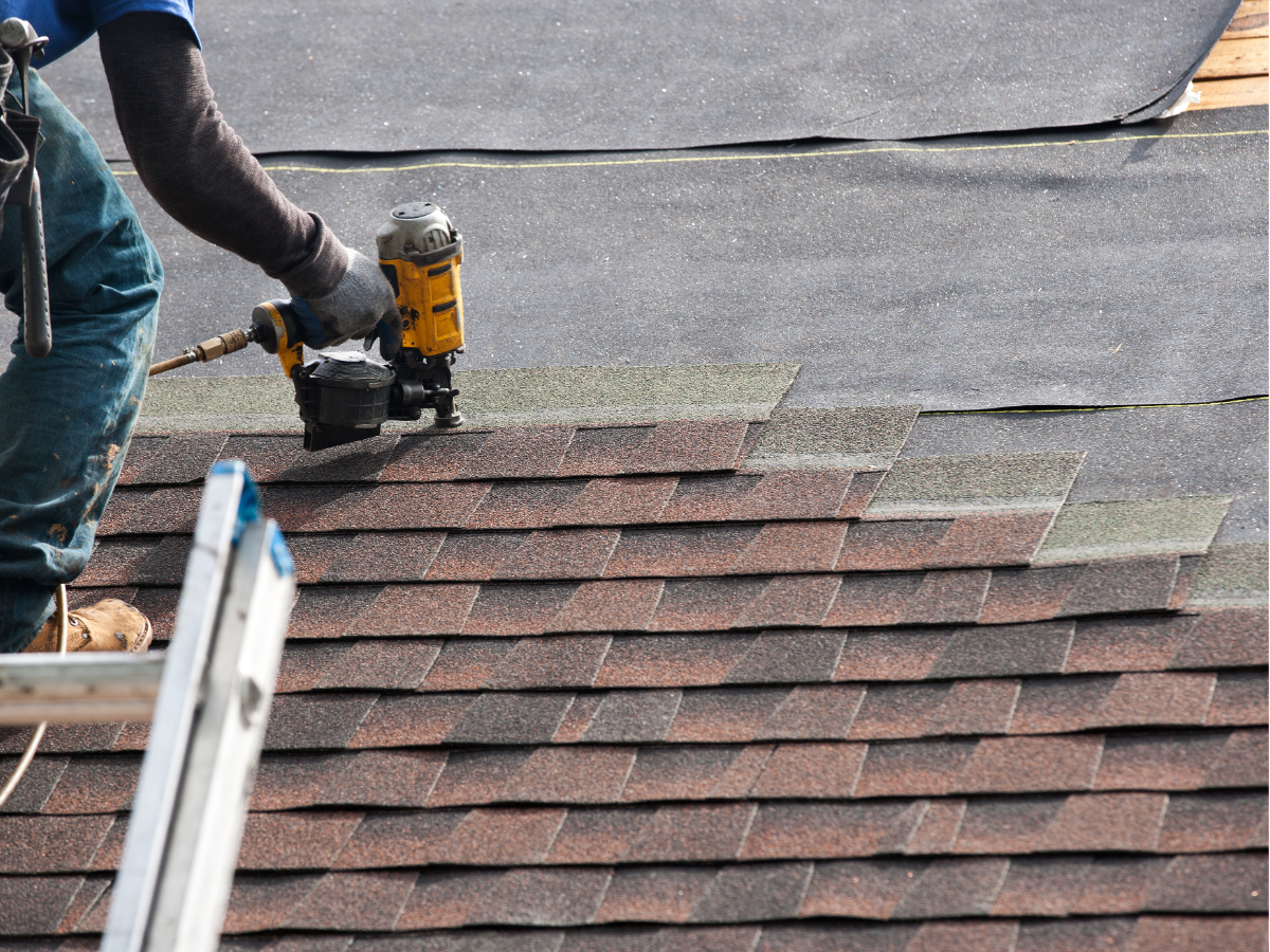 Roof partially replaced on a building, with exposed wood and black tiles. A crane assists with the work.