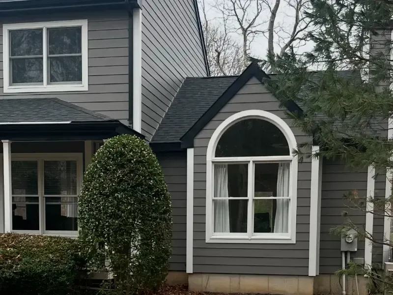 Gray house with white-trimmed windows and a unique arched window feature; dark roof, siding, and trim.
