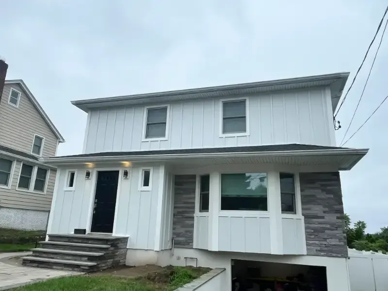 Two-story house with white siding and gray stone facade, under a cloudy sky. A garage is visible below.