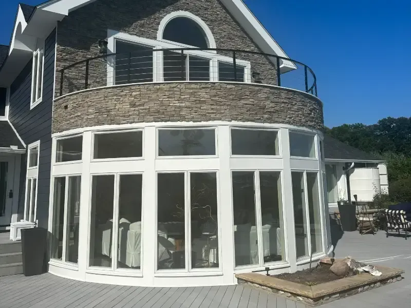 Curved, multi-window sunroom with gray stone accents and balcony on a modern home.