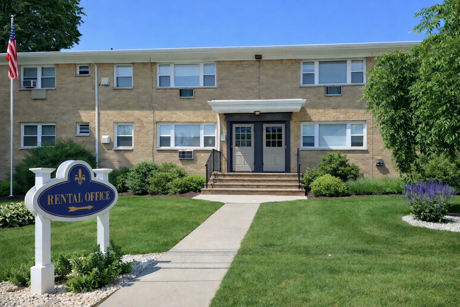 Rental office in a two-story brick apartment building with a sign and American flag on a sunny day.