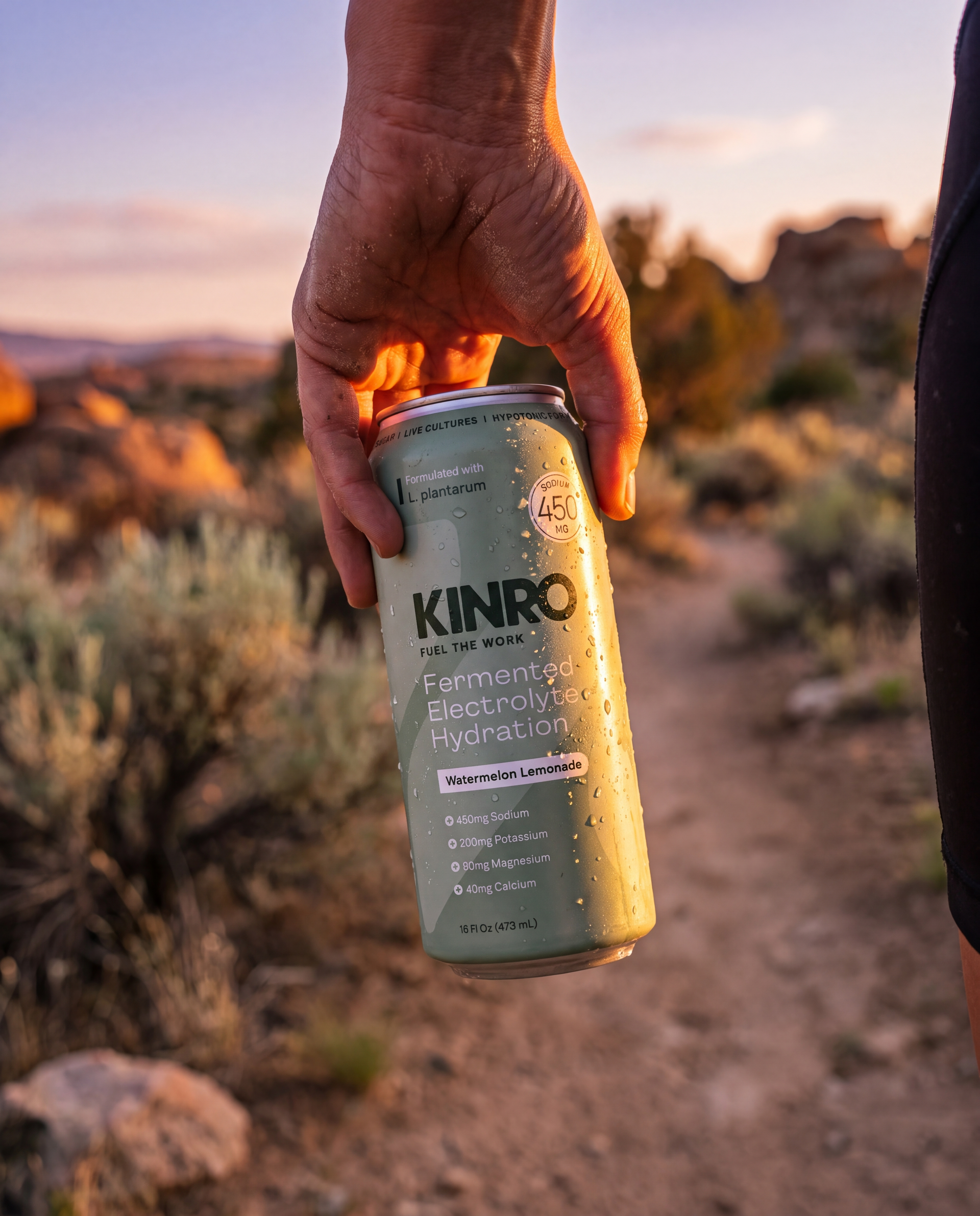 Hand holding a Kinroo can on a desert trail at sunset.