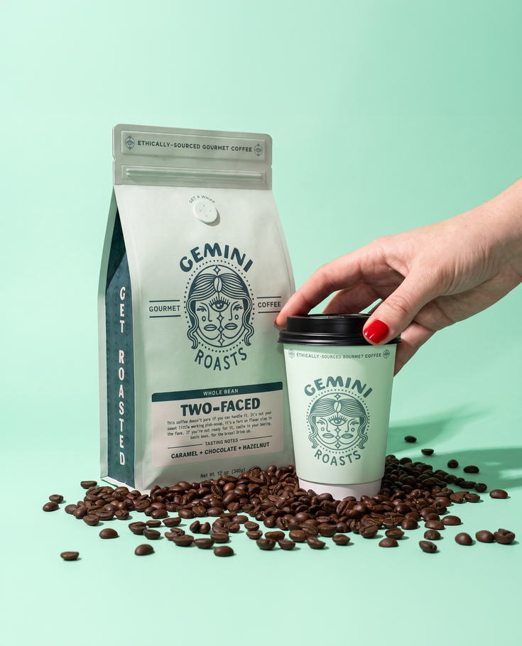 White coffee bag and cup with beans on mint background, hand placing red lid on the cup.