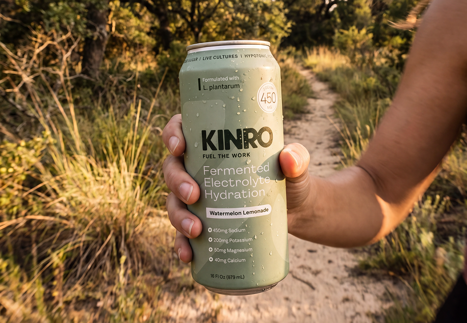 Hand holding a Kinro hydration can in a sunlit outdoor field of tall grass