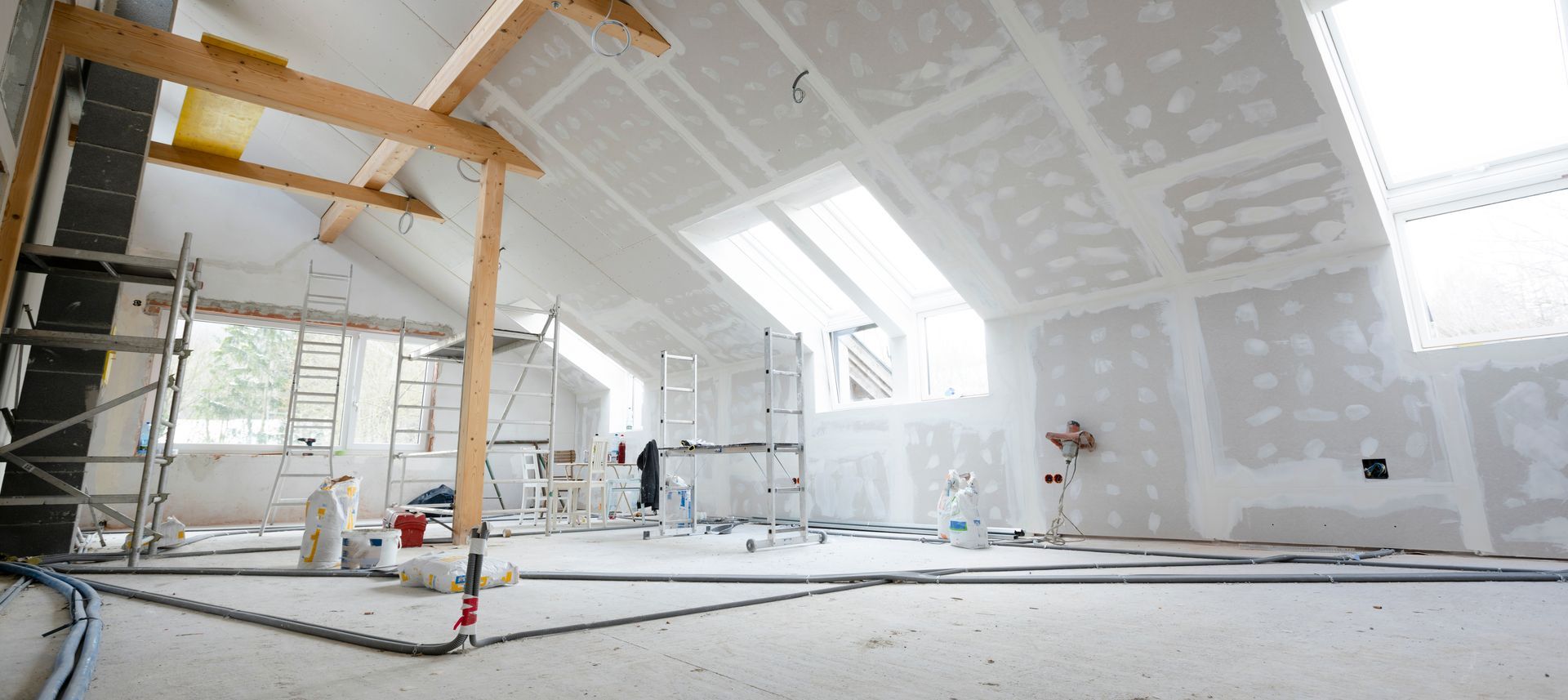 Renovation in progress inside a bright, unfinished room with scaffolding, drywall, and construction tools